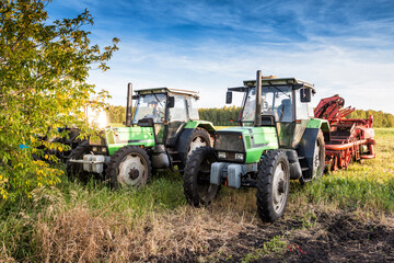 Modern wheeled agricultural tractors with harvesting equipment on an field