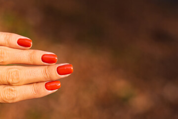 Close outdoor shot of womans hands in park orange color manicure, autumn mood. 