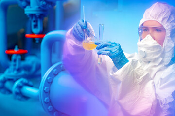 Hazardous industry. Laboratory assistant in chemical production. Woman in a protective suit examines chemical liquids in test tubes. The chemist evaluates the quality of raw materials for production.