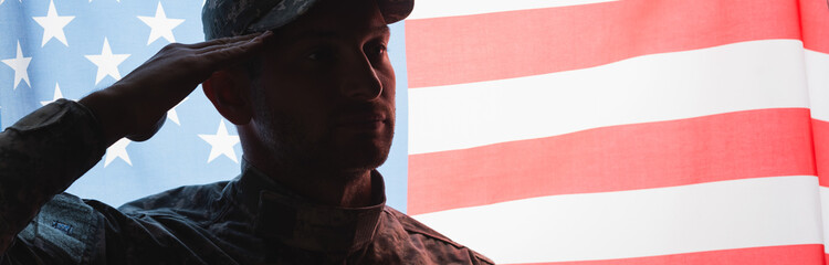 patriotic military man in uniform and cap giving salute near american flag on background, banner