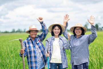 A group of three Asian farmer women stood smilingly and raised their hands at the green rice field.
