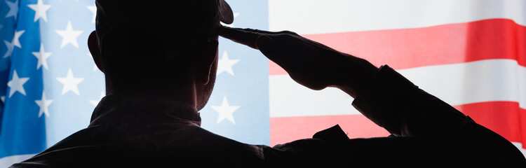 back view of patriotic military man in uniform giving salute near american flag on background,...