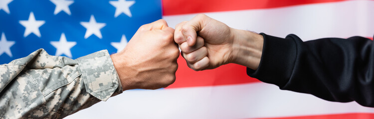 cropped view of soldier fist bumping with civilian man near american flag on blurred background,...