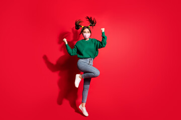 Photo of brown haired pigtails pretty lady celebrate jump wear green sweater jeans mask isolated on red color background