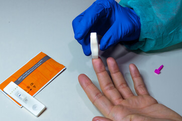 Hands of a nurse with individual protection equipment and patient, in the process of blood collection to make a rapid test for covid-19(coronavirus), in a hospital ward with sanitary elements.