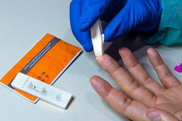 Hands of a nurse with individual protection equipment and patient, in the process of blood collection to make a rapid test for covid-19(coronavirus), in a hospital ward with sanitary elements.