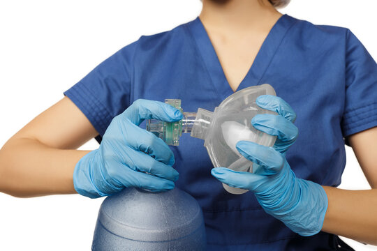 Young beautiful female doctor in blue surgical gown and gloves collects for use Am-bu bag for artificial lung ventilation isolated on white