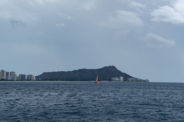 Waikiki, Honolulu, Oahu, Hawaii - February 9, 2019: A colorful red and yellow sailboat pops out in contrast to the grayish day with the volcanic crater Diamond Head in the background.  - obrazy, fototapety, plakaty