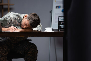 tired military man in uniform sleeping near cup in office
