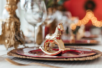 Glasses, plates and a figurine of a golden horse stand on a festively decorated table for Christmas dinner
