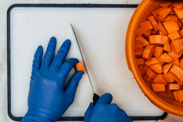 A man in blue gloves cuts sweet potato