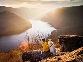 woman and her dog sitting on rock enjoying amazing autumn view over lake at sunset