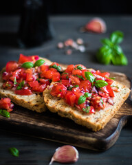 Bruschetta with tomatoes, garlic, and basil served on crispy bread. Dark background and herbs.