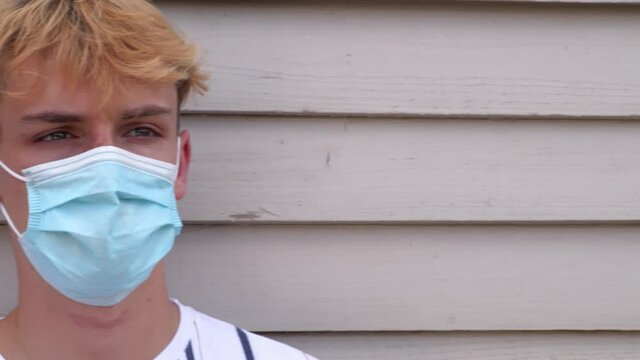 Panning shot of teenage boy young man wearing face mask outside during Coronavirus COVID-19 Pandemic