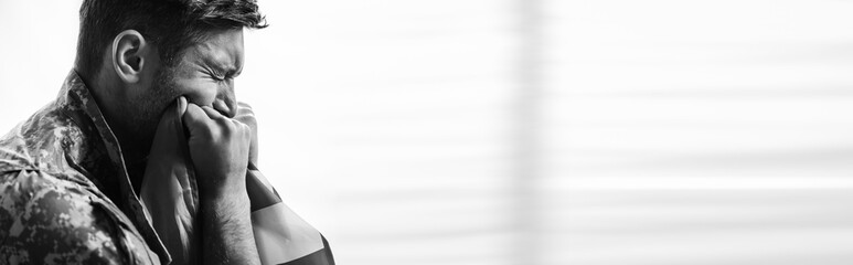 side view of military man in uniform crying while holding flag of america, banner