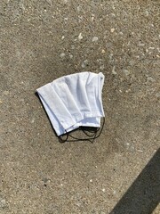 A close up of a dirty white face mask is discarded and laying on the side walk. This is a common scene as civilians amplify their efforts to protect themselves during the COVID-19  pandemic.