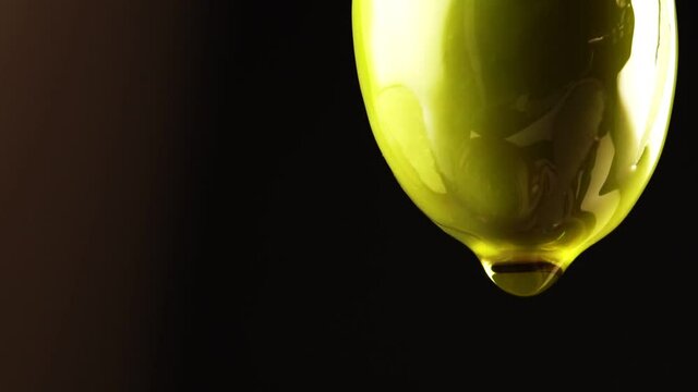 Drop of olive oil drips from green olive.