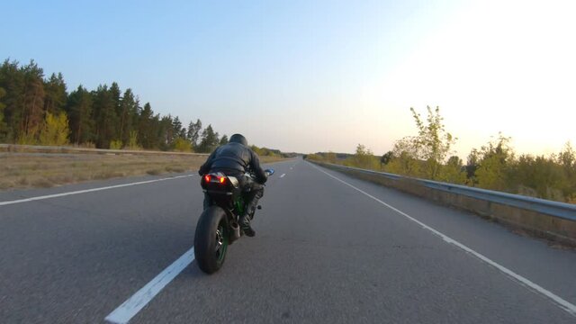 Follow to biker riding on modern sport motorbike on country road at sunset. Motorcyclist racing his motorcycle at highway. Guy driving bike during trip. Concept of journey and freedom. Aerial shot