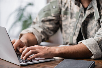 Cropped view of military man using laptop on desk - obrazy, fototapety, plakaty