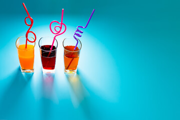 Variety of fruit juices in glasses with straws on blue background with copy space.