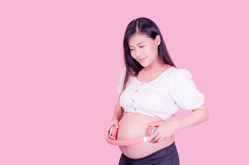 A beautiful pregnant Asian woman stands relaxed and has her unborn child listen to music with headphones connected to the Internet