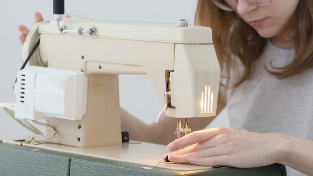 Girl sewing protective medicine mask on sewing machine at home to prev