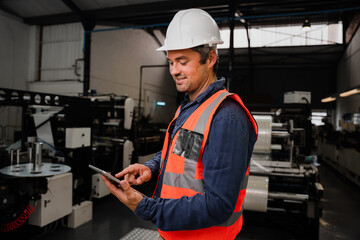 Smiling male engineer wearing uniform scrolling on tablet standing in factory