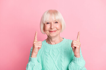 Photo portrait of pretty old lady pointing up at blank space smiling isolated on pastel pink color...