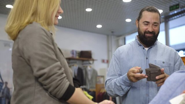 Portrait of positive confident Caucasian husband giving paying card to wife. Happy Caucasian woman buying clothes in shopping center with spouse. Purchasing and trading concept.