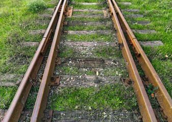 Obraz premium Old rusty, metal rails and wooden sleepers on a dirt surface with green grass. Railroad for passenger and freight trains. Photo, top view.