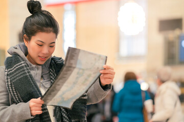 young asian female traveller sight seeing and enjoy advanture moment hand hold map with background of grand station and blur crowd people background