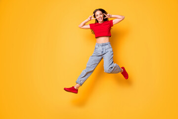 Fototapeta na wymiar Full size photo of cute jumping lady showing v-sign symbols wear red crop top jeans shoes isolated yellow color background