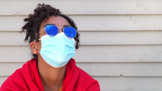 Beautiful mixed race African American girl biracial teenager young woman outside wearing a face mask and sunglasses during COVID-19 Coronavirus pandemic