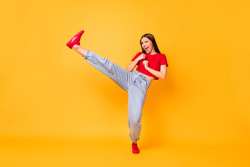 Full length photo focused girl practicing kicks raise leg exercise wear red crop top jeans isolated yellow color background