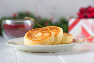 New Year's Christmas food: breakfast - cheese cakes, pancakes, raspberry jam on a background of fir branches with cones and red berries and a gift