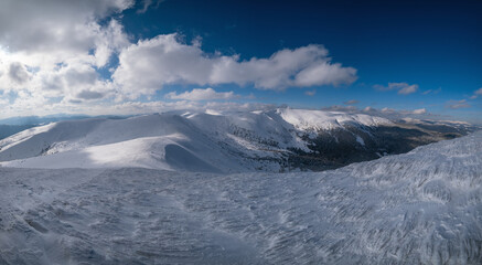 Snow and wind formed ice formations covered winter mountain plateau, tops with snow cornices in far. Magnificent sunny day on picturesque beautiful alpine ridge.