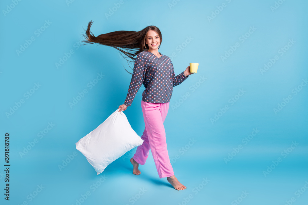 Wall mural Full length photo of charming teenager girl air blow long hairstyle barefoot hold cup pillow morning walk wear dotted shirt pink pants pajamas sleepwear isolated blue color background