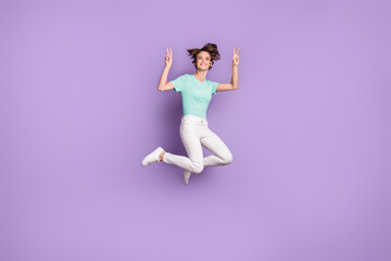 Fototapeta na wymiar Full size profile photo of cute optimistic girl jumping show v-sign wear white sneakers pants blue t-shirt isolated on violet background