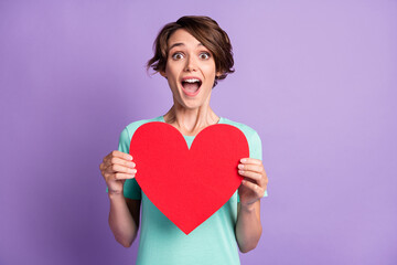 Photo of surprised young lady wear casual teal outfit holding big red heart isolated purple color background