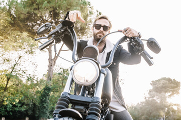 Man with rude expression wearing sunglasses and leaning against the handlebars of a motorcycle