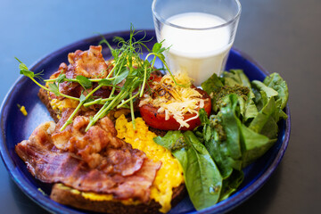 Very bright and healthy breakfast on a plate - bacon, egg, salad, tomato, cheese, a glass of yogurt. Close-up.
