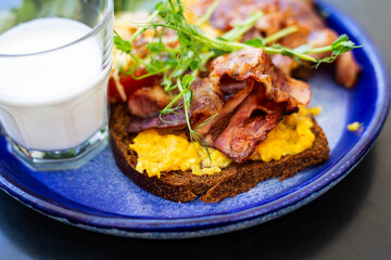 Very bright and healthy breakfast on a plate - bacon, egg, salad, tomato, cheese, a glass of yogurt. Close-up.