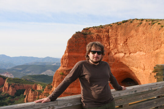 A man of European appearance with a beard and sunglasses poses against a background of red kog canyon.