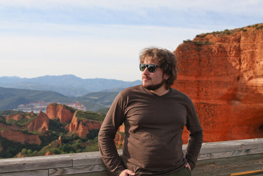 A man of European appearance with a beard and sunglasses poses against a background of red kog canyon.