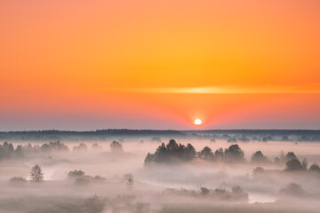 Amazing Sunrise Sunset Over Misty Landscape. Scenic View Of Foggy Morning Sky With Rising Sun Above Misty Forest And River. Early Summer Nature Of Eastern Europe