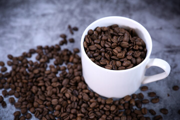 White cup full of coffee beans close up against the dark grey background. Coffee mug. Morning espresso.