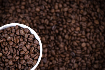 White cup full of coffee beans close up against the coffee beans background. Coffee mug. Morning espresso. 