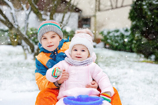 Little kid boy and cute toddler girl sitting together on sledge. Siblings, brother and baby sister enjoying sleigh ride during snowfall. Children sledding on snow. Active fun for family vacation