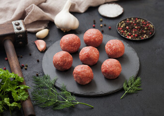 Fresh raw minced beef meatballs on round board with pepper, salt and garlic on black background.