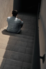 A young guy sits on the steps, view from the back. Underpass, stairs down.